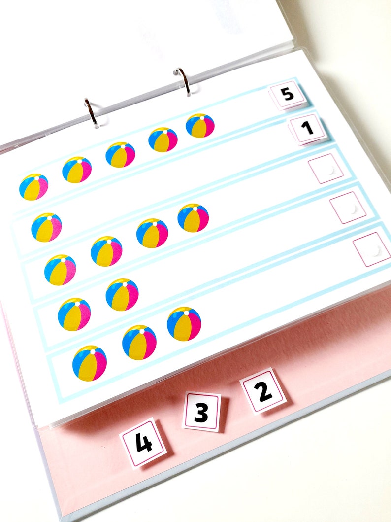 May include: A colorful learning activity with a binder and pages featuring beach ball images and number cards. The numbers 1, 2, 3, 4, and 5 are visible.