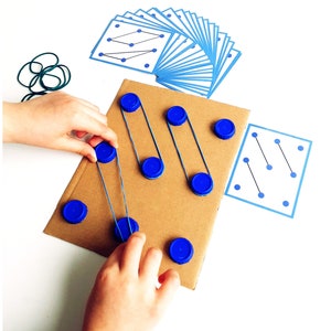 May include: A child's educational toy featuring a cardboard base with blue bottle caps and rubber bands. The toy includes cards with blue dot patterns and a set of green rubber bands. The child is interacting with the toy.