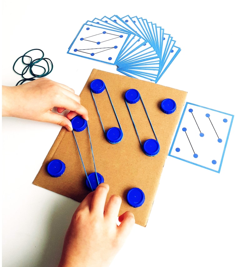 May include: A child's educational toy featuring a cardboard base with blue bottle caps and rubber bands. The toy includes cards with blue dot patterns and a set of green rubber bands. The child is interacting with the toy.