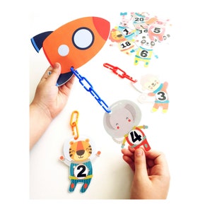 May include: A colorful educational toy set featuring a rocket, a chain, and animal characters with numbers 1 through 20. The animals are dressed as astronauts and include a tiger, elephant, panda, and rabbit.