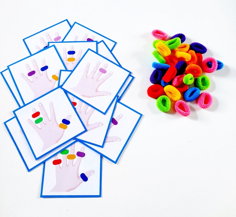 K&ouml;nnte beinhalten: Ein Satz bunter Handabdruckkarten mit verschiedenen farbigen Punkten auf jedem Finger. Die Karten sind f&uuml;r ein Zuordnungsspiel mit bunten Gummib&auml;ndern konzipiert.