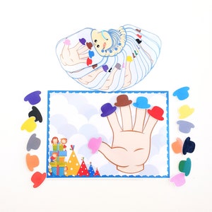 May include: A colorful felt finger puppet game with a hand and five fingers, each with a different colored hat. The hats are red, blue, green, yellow, and brown. There are also extra hats in the image.