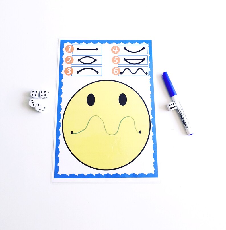 May include: A learning activity sheet with a large yellow smiley face and a green line. The sheet has numbered line patterns and is accompanied by dice and a blue marker. The sheet has a blue border.