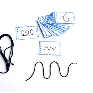 May include: A set of blue and white cards with different line patterns, including a wavy line, a squiggly line, and a circle. There are also two pieces of black string, one in a circle shape and the other in a wavy line shape.