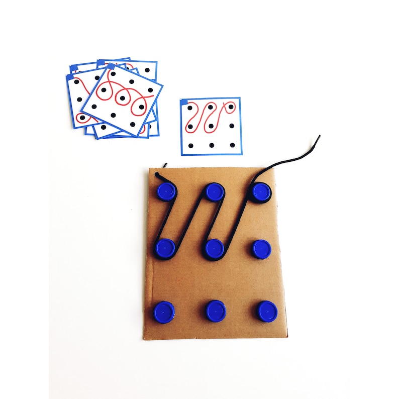 Op de afbeelding: Een kartonnen spelbord met blauwe dopjes en zwart touw. Het touw wordt door de dopjes geregen om een ​​labyrintpatroon te cre&euml;ren. Er zijn ook verschillende witte kaarten met zwarte stippen en rode lijnen.