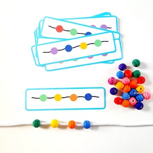 May include: A set of colorful bead threading cards with a string of beads in the colors shown on the cards. The cards have a blue border and a black line with circles representing the beads. The beads are green, yellow, orange, blue, purple, and red.