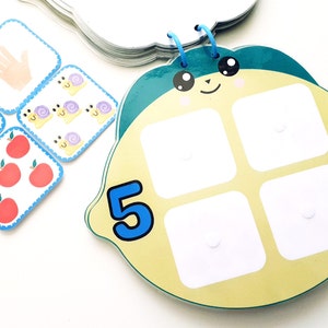 Könnte beinhalten: Ein gelbes und grünes, limonenförmiges Lernspielzeug mit einer blauen Zahl "5" und vier leeren Feldern. Das Spielzeug ist für Kinder konzipiert, um Zählen und Zuordnen zu lernen.