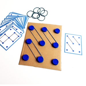 May include: A brown cardboard game board with blue bottle caps and rubber bands. Several blue and white cards with dot patterns are arranged around the board. A set of green rubber bands is also included.