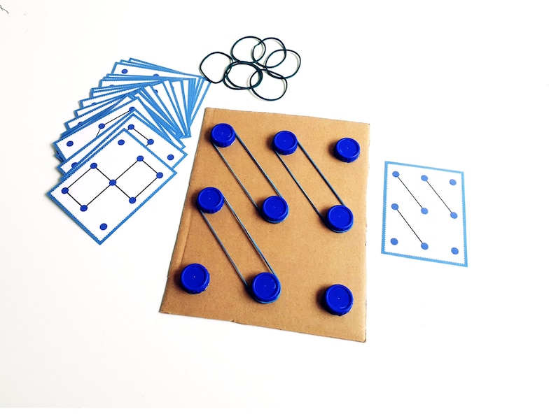 May include: A brown cardboard game board with blue bottle caps and rubber bands. Several blue and white cards with dot patterns are arranged around the board. A set of green rubber bands is also included.