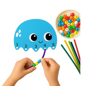 Op de afbeelding: Een blauw, kwalvormig educatief speelgoed met de nummers 1-5. Een kind rijgt kleurrijke kralen op een paarse draad, passend bij de nummers. Een mandje met kralen en gekleurde stokjes is ook aanwezig.