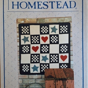 May include: A quilt pattern titled "Liberty Homestead" with a checkerboard design, stars, and hearts. The quilt is set against a brick wall, with a wooden box and a metal basket in the foreground. The text "Liberty Homestead" is displayed above the quilt.