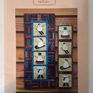 May include: A paper foundation pattern for a set of four snowman ornaments or a wall quilt. The design features snowmen on skis and snowboards, with a variety of colorful fabric patterns. The MH Designs logo is at the top.