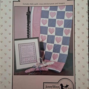 May include: A framed cross-stitched poem, baby quilt, and hangers are featured in this image. The quilt has a checkerboard pattern with pink hearts on a blue and white background. The image is framed with a pink border and includes the text "Sometime".