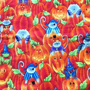 Puede incluir: Un patrón de tela con calabazas naranjas con caras talladas y hojas verdes, intercaladas con ilustraciones de gatos azules y ranas verdes que usan sombreros de bruja, capas y parches en los ojos, creando una escena densa de Halloween.