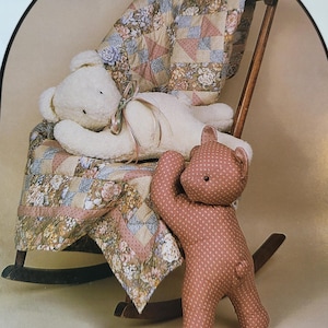 May include: Two plush teddy bears, one white and one brown with white polka dots, sitting on a rocking chair with a floral patterned quilt.