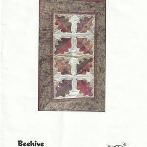 May include: A rectangular quilt titled "Fair Oaks," measuring 20" x 30". The quilt features a central design of stylized oak leaves in shades of red, brown, and cream, set against a cream background. The border is a floral pattern.