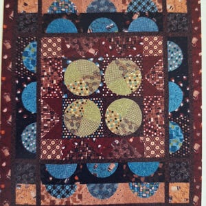 May include: A patchwork quilt with a complex design featuring various patterns and colors. The quilt incorporates half-circle and circular shapes in shades of blue, green, and brown, set against a dark red background. The quilt has a repeating pattern of coffee pots. The number #0956 is in the bottom right corner.