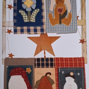 May include: A set of six handmade quilted wall hangings featuring a variety of designs, including a flower, a bunny, a pumpkin, a snowman, and a bell. The hangings are displayed on a wooden ladder with a star-shaped ornament at the top.