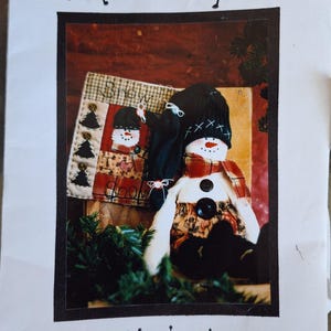 May include: A handcrafted snowman doll with a black hat, scarf, and button details. The image also features a small decorative banner with a snowman design and the text "Snow". The text "Colorado Country Crafts" is at the top.