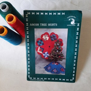 May include: A green book with the title "Amish Tree Skirts" and a picture of a red and blue patchwork tree skirt. The book is from "Tomorrow's Heirlooms" and is copyrighted 1988.