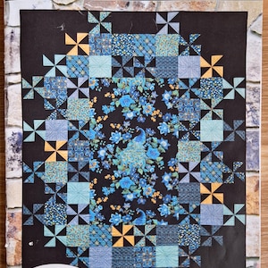 Peut inclure: Une couverture de patron de quilt avec un motif géométrique de carrés et de formes d'éoliennes en bleu, sarcelle et or sur un fond noir. Le centre présente un paon et un motif floral. Le texte "Grand Central" et "Swirly Girls" sont visibles.