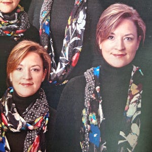 Può includere: Diverse donne indossano dolcevita neri e sciarpe fantasia. Le sciarpe presentano disegni floreali in rosso, blu e bianco su sfondo nero. Le sciarpe sono drappeggiate attorno al collo.