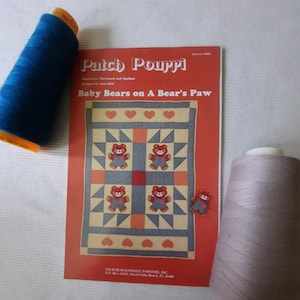 Puede incluir: Un patrón de colcha de retazos rojo y blanco con el título "Baby Bears on A Bear's Paw" y el texto "Patch Pourpi" impreso en el frente. El patrón es para patchwork y aplique y está diseñado por Jean Eitel.