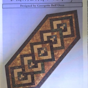 May include: A quilt pattern titled "Diamond Medley" by Georgette Dell'Orco. The design features a repeating geometric pattern in shades of brown, tan, and green. The finished size is 26 inches by 68 inches.