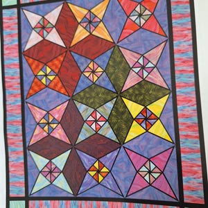 May include: A quilt with a geometric pattern of stars in various colors, including red, blue, green, yellow, and pink. The stars are made up of smaller triangles and squares, creating a stained glass effect.