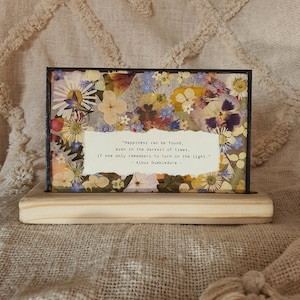 May include: A framed pressed flower art piece with a quote by Albus Dumbledore: "Happiness can be found, even in the darkest of times, if one only remembers to turn on the light." - Albus Dumbledore -
