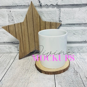 Peut inclure: Une tasse en céramique blanche sur un dessous de verre en bois. La tasse est posée sur une surface en bois blanchi à la chaux avec une étoile en bois derrière elle. Le texte "Divine Mockups" est visible en rose.