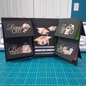 Può includere: Un porta carte regalo nero con più tasche. Ogni tasca ha un design metallico e testo, tra cui "Dinner Out", "Retail Therapy", "Fuel Up" e "Snack Attack". Il centro presenta cappelli di laurea. Il porta carte è aperto, rivelando carte regalo.
