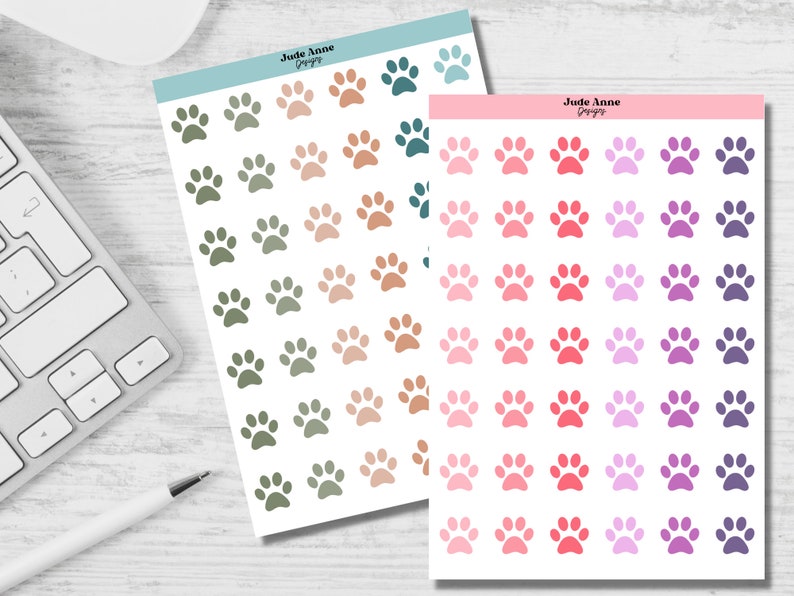 May include: Two sheets of paw print stickers. The first sheet has green, brown, and beige paw prints. The second sheet has pink, red, purple, and lavender paw prints. The sheets are labeled "Jude Anne Designs".