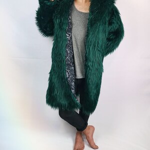 May include: A long, dark green faux fur coat with a hood. The lining of the coat is a black and white print of a celestial design.