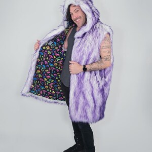 May include: A sleeveless faux fur vest featuring a purple and white gradient pattern with an attached hood. The interior lining is black and decorated with a colorful, repeating pattern of various mushrooms in shades of pink, yellow, and blue.