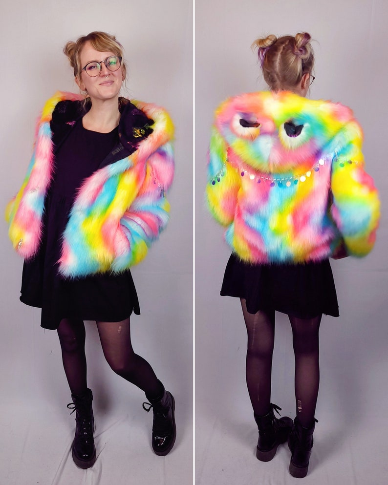 May include: A rainbow-colored faux fur jacket with a hood featuring a sequined eye design. The jacket is cropped and has a relaxed fit.