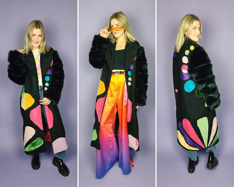May include: A black long coat with colorful abstract shapes and fur trim on the sleeves. The coat is worn over a rainbow ombre pants.