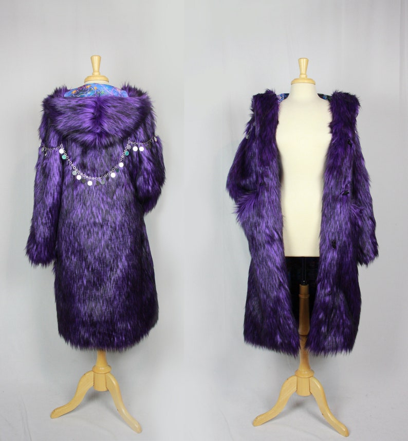 May include: Purple faux fur coat with a hood and a chain of silver charms around the neckline. The coat is on a wooden mannequin.