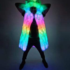 May include: A long, sleeveless faux fur vest featuring an integrated hood with animal-like ears. The garment is illuminated with vibrant, multi-colored LED lights that transition through shades of green, pink, and blue across the entire surface.