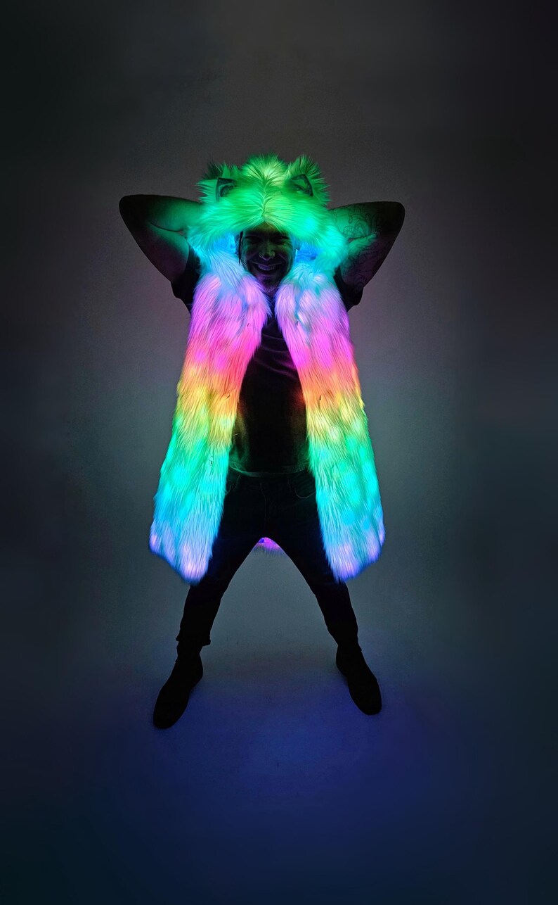 May include: A long, sleeveless faux fur vest featuring an integrated hood with animal-like ears. The garment is illuminated with vibrant, multi-colored LED lights that transition through shades of green, pink, and blue across the entire surface.