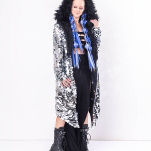 May include: A silver sequined coat with a black faux fur hood and lining. The coat has a long, flowing silhouette and is worn over a black skirt.