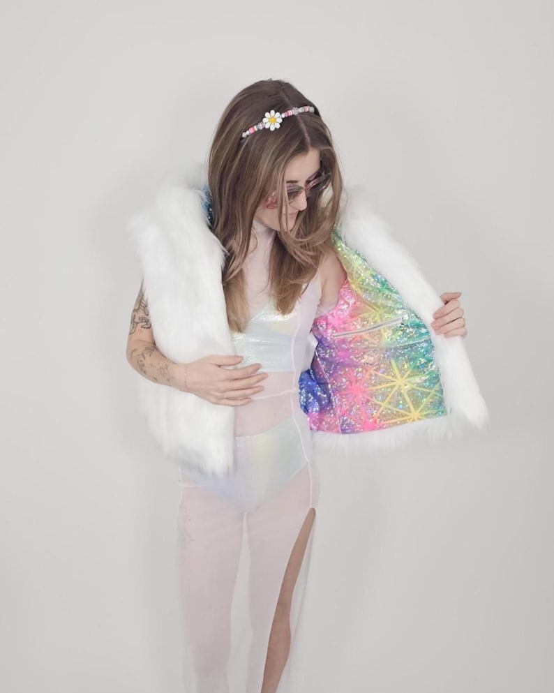 May include: A white faux fur vest featuring a vibrant, multicolored holographic interior lining with a geometric star pattern. The vest is worn over a sheer, iridescent white bodysuit with high side slits and a matching daisy headband.