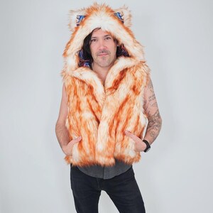 May include: A sleeveless vest made of orange and white faux fur featuring an attached hood with pointed ears. The interior lining of the hood displays a colorful, intricate paisley pattern in shades of blue, red, and gold. The vest has two front pockets.