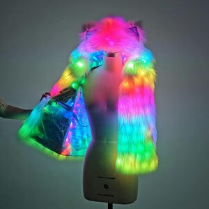 May include: A sleeveless faux fur vest with an integrated hood featuring animal-like ears. The garment is illuminated by vibrant, multi-colored LED lights that transition through shades of pink, blue, green, and yellow across the plush texture.