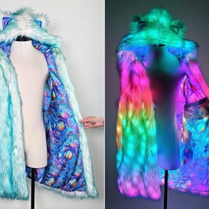 May include: A long-sleeved faux fur coat featuring a hood with ears, rendered in light blue. The interior lining displays a vibrant, multicolored psychedelic pattern. The coat is equipped with integrated LED lights that glow in pink, green, and blue.