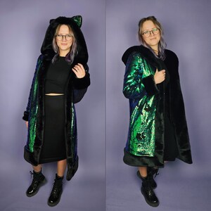 May include: A long black and green sequined coat with a faux fur trim and a hood. The hood has cat ears.