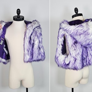May include: A sleeveless faux fur vest featuring a hooded design with long, shaggy white and purple-tipped fibers. The interior is lined with a solid purple fabric and includes a small rectangular pocket on the inner left side with a patterned label.