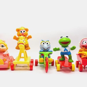 Peut inclure: Un ensemble de six figurines de personnages de Sesame Street, chacun conduisant un véhicule jouet différent. Les personnages incluent Big Bird, Cookie Monster, Elmo, Bert, Ernie et Grover. Les véhicules incluent une voiture, un cheval à bascule, un tricycle, une planche à roulettes, une charrette et une trottinette.