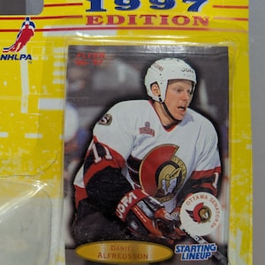 May include: A hockey card featuring Daniel Alfredsson of the Ottawa Senators. The card is from the 1997 Fleer 10th Year Edition set. The card is yellow with a red border and features a photo of Alfredsson in his Senators uniform. The card also includes the text "Starting Lineup" and "Ottawa Senators".