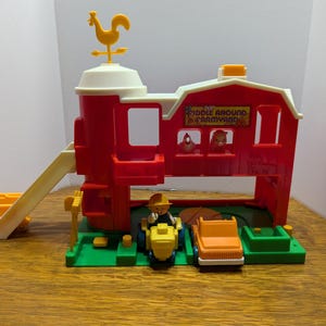 May include: A red plastic toy barn with a yellow rooster on top. The barn has a slide, a small truck, and a figure of a farmer. The text "Kiddle Around Farmyard" is printed on the front of the barn.